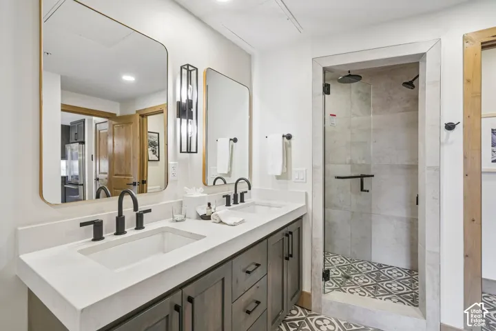 Bathroom featuring a dual-sink vanity with matte black fixtures, rectangular integrated basins, geometric patterned floor tiling, and a walk-in shower with a glass enclosure