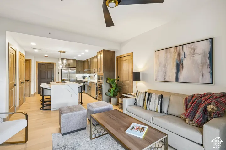 Kitchen featuring stainless steel appliances, a waterfall-edge island, wood-finish cabinetry, and recessed lighting, complemented by wood-finish flooring throughout