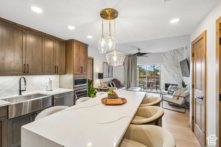Kitchen featuring a quartz waterfall island, custom wood cabinetry, farmhouse-style stainless steel sink, geometric pendant lighting, and a fireplace with floor-to-ceiling surround