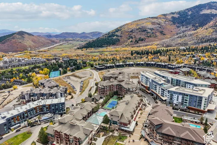 Aerial perspective of a multi-structure property complex featuring exterior stone and wood-finish siding, multi-pitch rooflines, surface tennis courts, and swimming pools, set against a mountainous backdrop