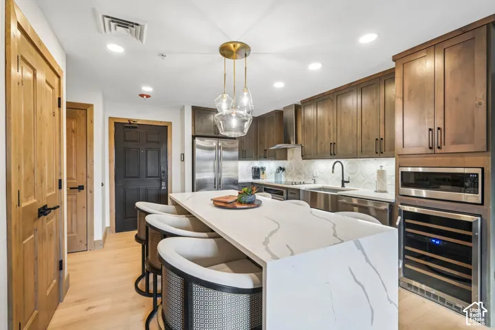 Kitchen featuring custom wood cabinetry, an expansive quartz island with waterfall edge, stainless steel appliances including a built-in wine cooler, and glass pendant lighting