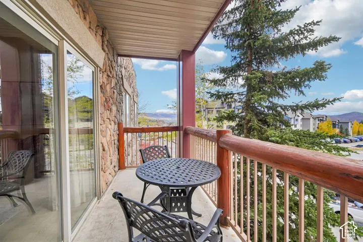 Covered balcony featuring stone exterior cladding, horizontal log railing, and large sliding glass doors