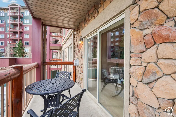 Covered outdoor balcony featuring stone veneer wall cladding, a wood-post railing, and glass sliding door access