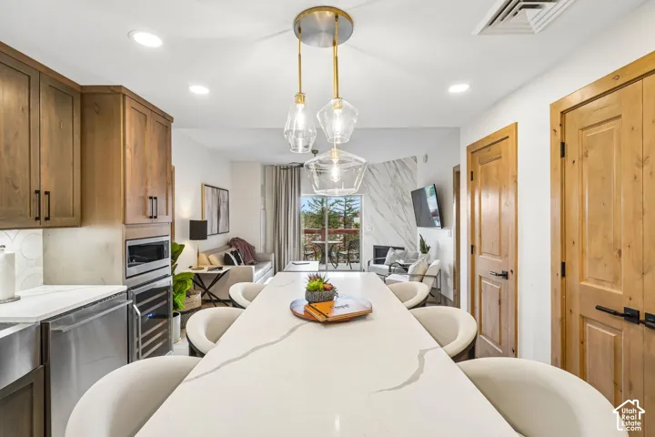 Large island with a stone-finish countertop, wood cabinetry, stainless steel appliances, multi-pendant lighting, and stone-finish fireplace surround