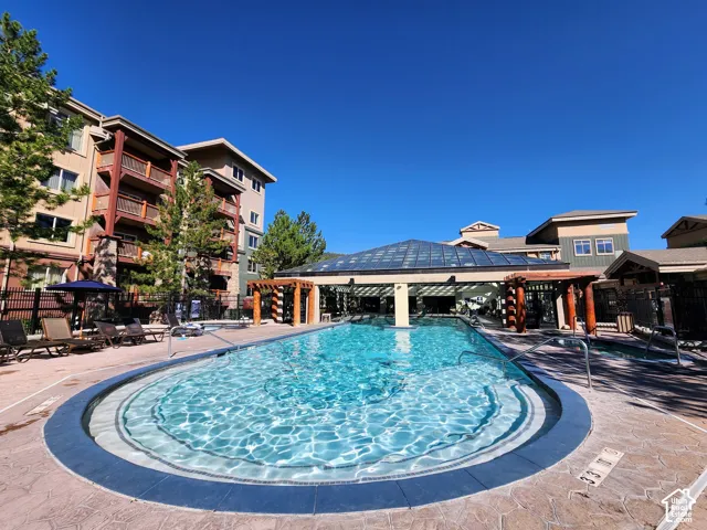 Swimming pool with a glass-enclosed pavilion, stone-tile decking, timber pergola structures, and integrated hot tub