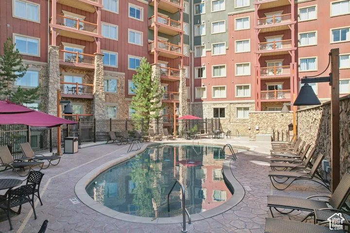Outdoor pool surrounded by stamped concrete decking, stone-faced structural pillars, and multi-story building facade with private balconies