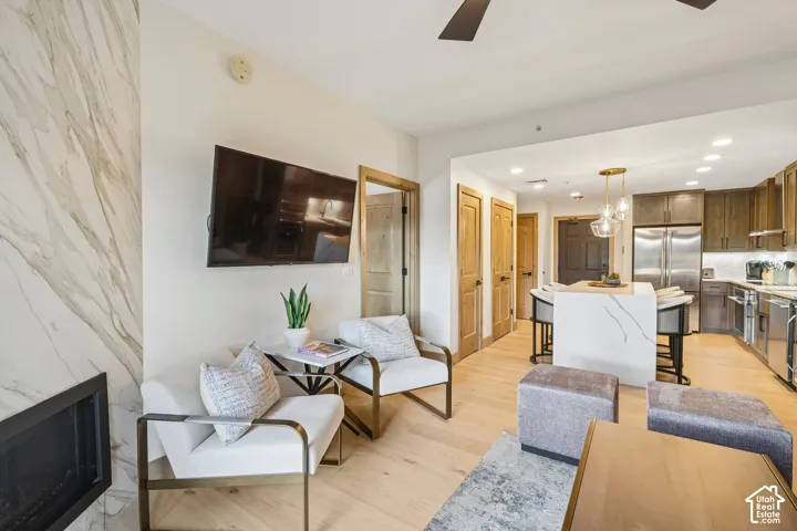 Fireplace featuring floor-to-ceiling stone-finish surround, wood-finish flooring, kitchen island with stone-finish waterfall countertop, recessed lighting, and stainless steel kitchen appliances