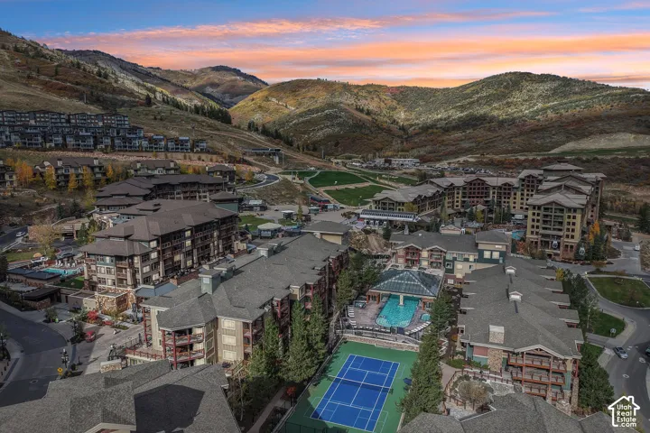 Mountain-side residential complex featuring an outdoor swimming pool, tennis court, tiered multi-story architecture, and surrounding hillside landscape