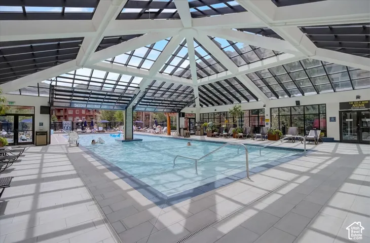 Indoor swimming pool featuring an expansive glass-paneled gabled roof, tile flooring, and metal handrails