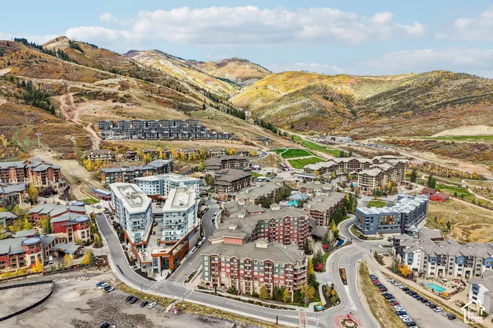 Aerial perspective of a multi-structure mountain community featuring complex rooflines, masonry and timber exterior detailing, paved road infrastructure, and mountainous terrain surroundings
