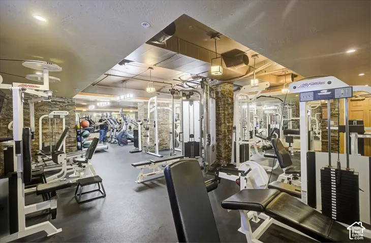 Fitness room featuring stone-cladding, rubber flooring, mirrored walls, recessed lighting, and industrial-style pendant fixtures