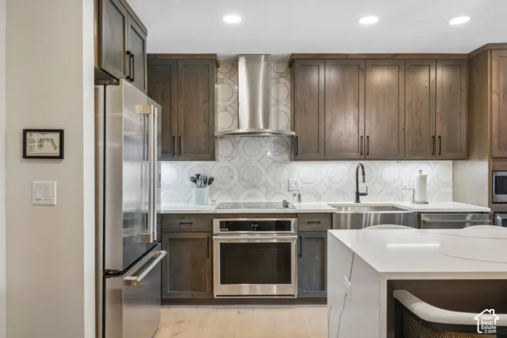Kitchen featuring dark wood-finish cabinetry, white solid-surface countertops, a geometric-patterned backsplash, stainless steel appliances, and an undermount sink with a matte black faucet