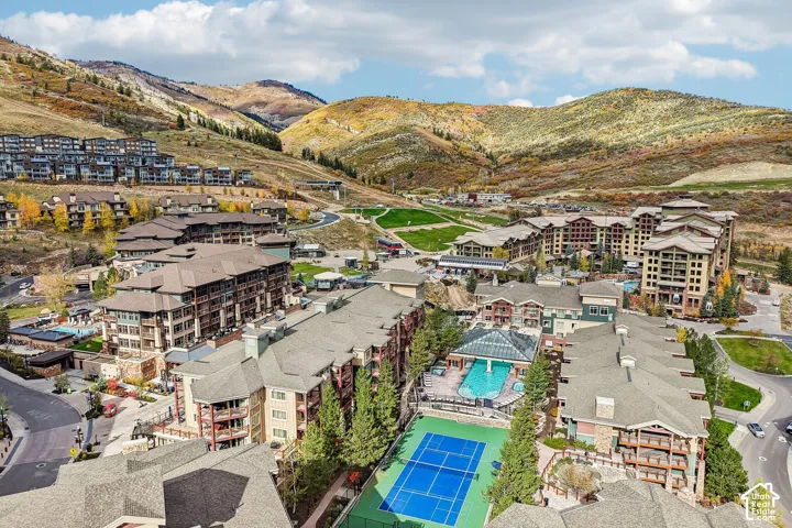 Aerial perspective of a multi-structure mountain resort community featuring a tennis court, swimming pool, and hillside terrain