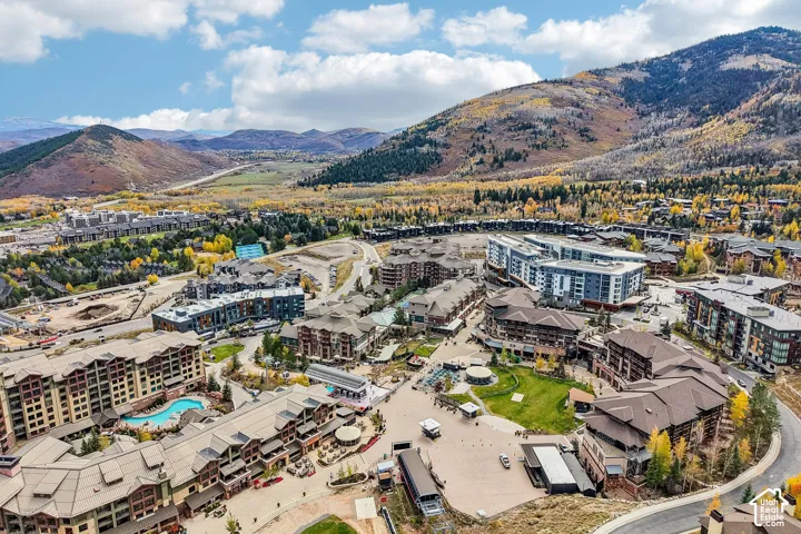 Aerial perspective of a mountain resort community featuring multi-story stone and timber-clad structures, landscaped green spaces, a swimming pool, and proximity to expansive mountain terrain