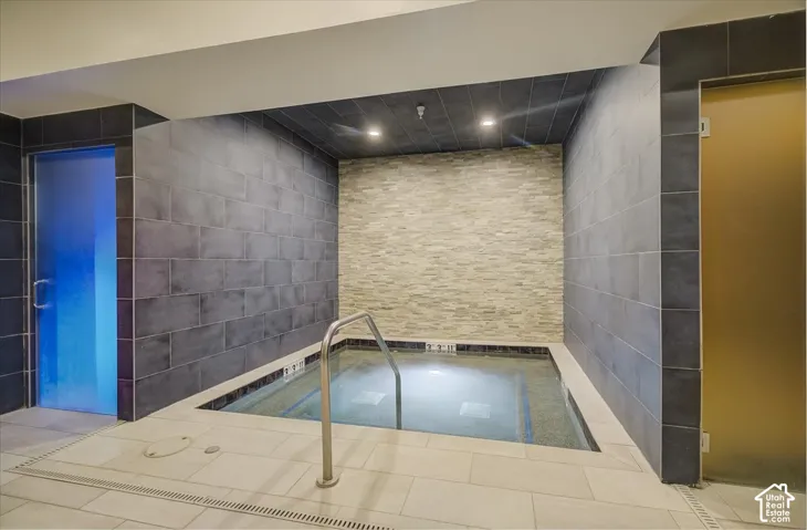 Indoor spa featuring an inset plunge pool with a stainless steel grab bar, textured stone accent wall, large-format tile surround, and recessed ceiling lighting