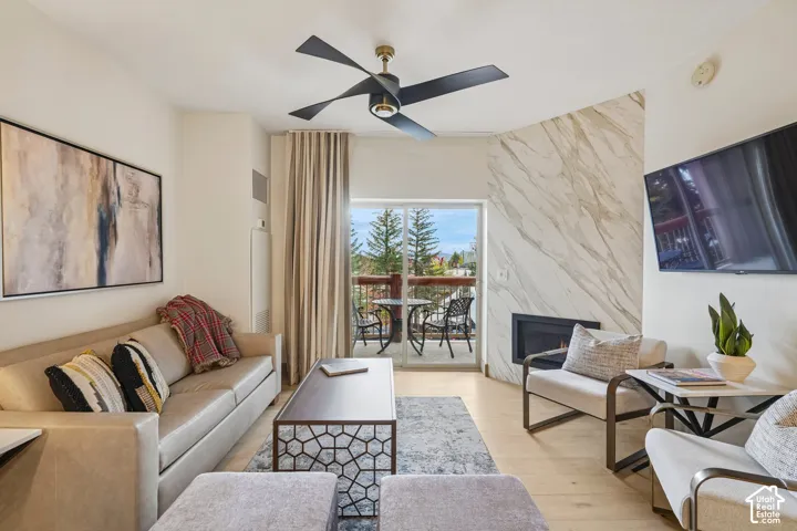 Living area featuring wood-finish flooring, a contemporary ceiling fan, and a floor-to-ceiling stone-surround fireplace