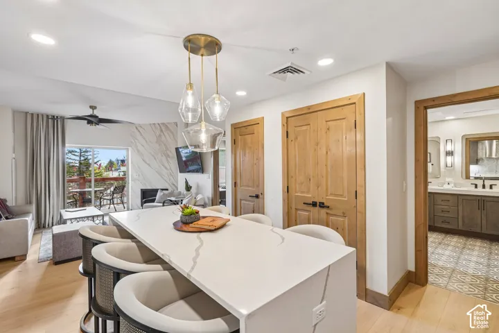 Kitchen island with a waterfall-edge quartz countertop, pendant lighting, wood-finish flooring, natural wood doors with matte black hardware, and a stone-clad fireplace surround