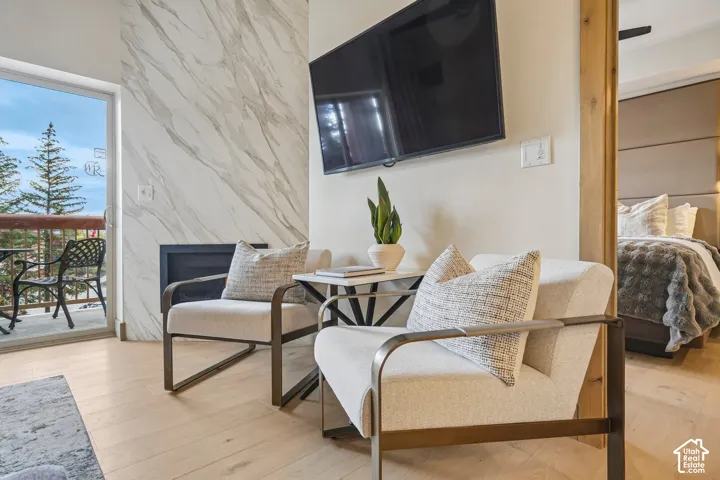 Fireplace feature wall with stone-finish cladding, light-toned wood-finish flooring, and sliding glass door leading to a balcony