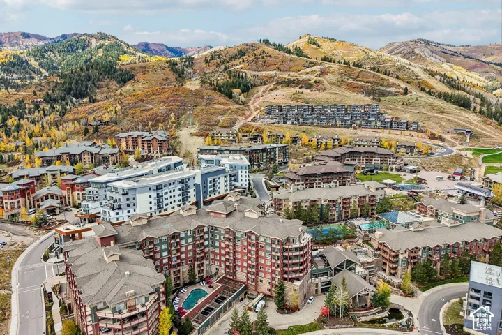 Aerial perspective of a mountain resort complex featuring multi-story residential buildings, outdoor swimming pools, tennis courts, and expansive surrounding mountain terrain