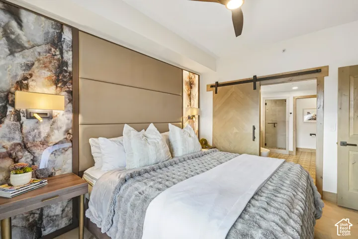 Floor-to-ceiling stone accent wall, custom upholstered headboard, chevron-patterned wood sliding barn door, and integrated wall-mounted lighting