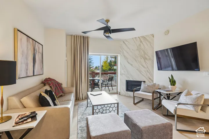 Living area featuring stone-surround fireplace, sliding glass door, modern ceiling fan, and light wood-finish flooring