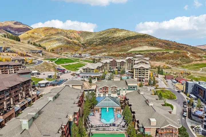 Aerial perspective of a multi-structure property featuring an outdoor swimming pool, a glass-enclosed atrium, stone and timber-style siding, and mountain terrain