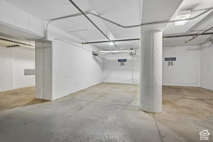 Covered parking space featuring concrete flooring, structural support columns, and overhead lighting