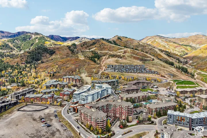Aerial perspective of a multi-structure residential community nestled within a mountainous landscape featuring slopes, varied foliage, and paved roadway infrastructure