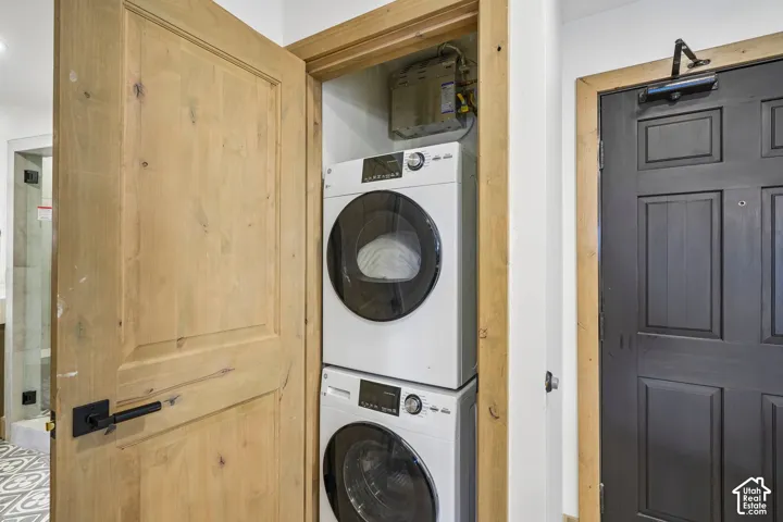 Laundry closet featuring a stacked front-load washer and dryer, natural wood-finished interior door with matte black hardware, and an industrial-style dark-finish door with an overhead hydraulic closer