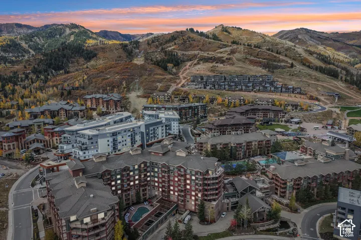 Aerial perspective of a mountain resort development featuring multi-story masonry and timber buildings, a central outdoor swimming pool, and immediate access to expansive mountainous terrain