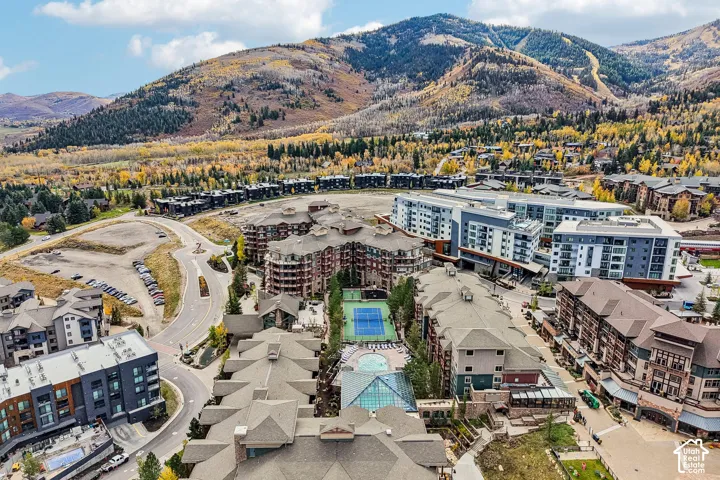 Aerial perspective of the residential complex featuring a tennis court, swimming pool, and mountain backdrop