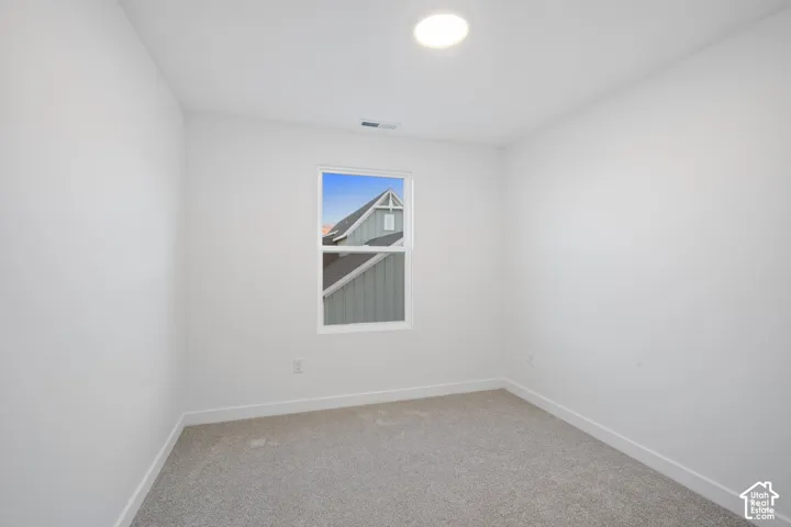 Neutral-toned carpeting, white walls, and a single-hung window featuring a view of neighboring architecture, illuminated by a recessed ceiling light