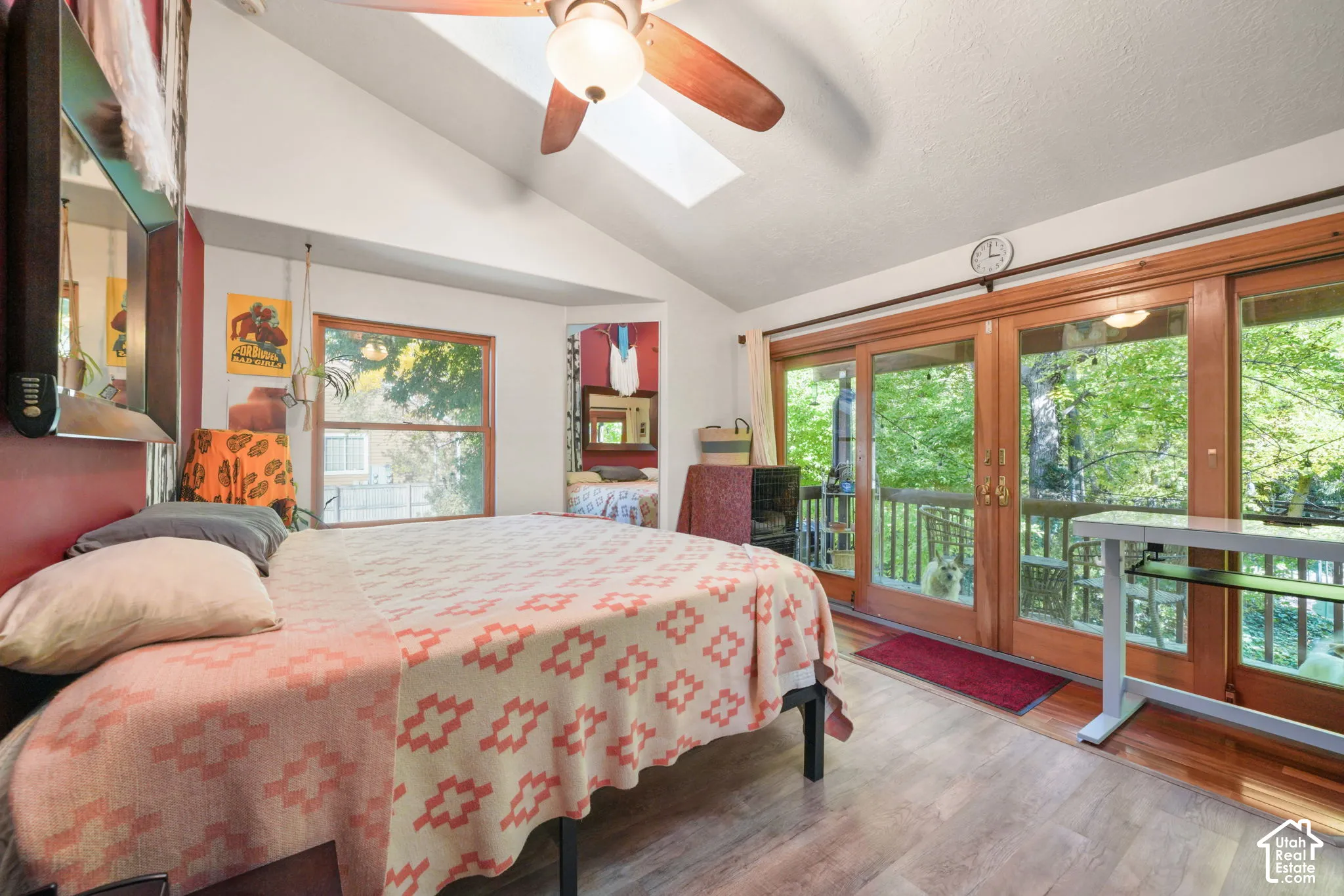 Vaulted ceilings featuring a skylight and a ceiling fan, wood-finish flooring, and multi-panel glass doors with wood trim
