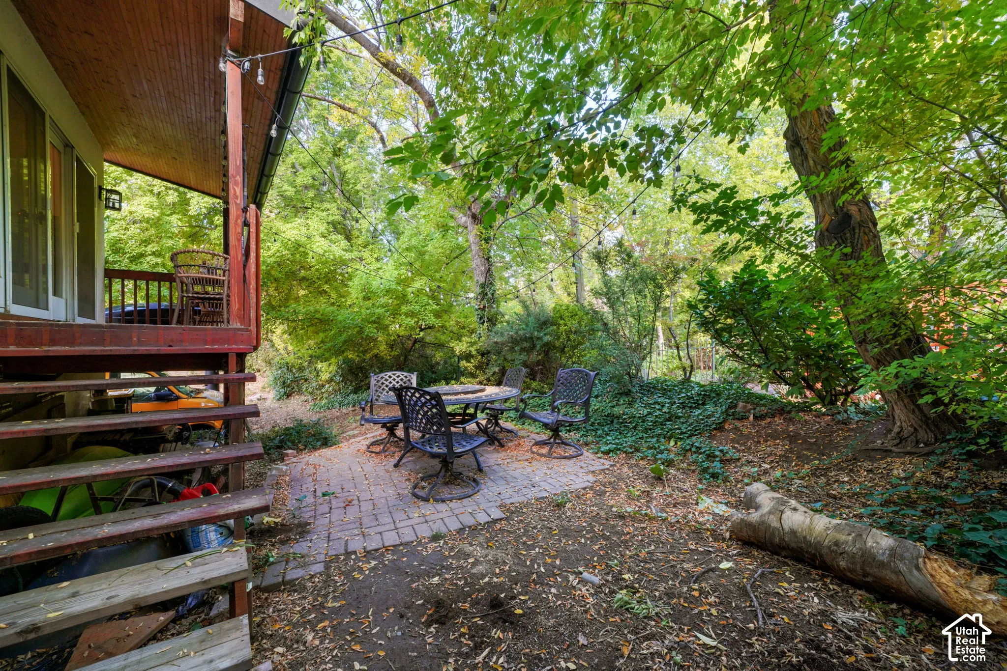 Backyard featuring a paved brick patio, elevated wooden deck, and mature trees