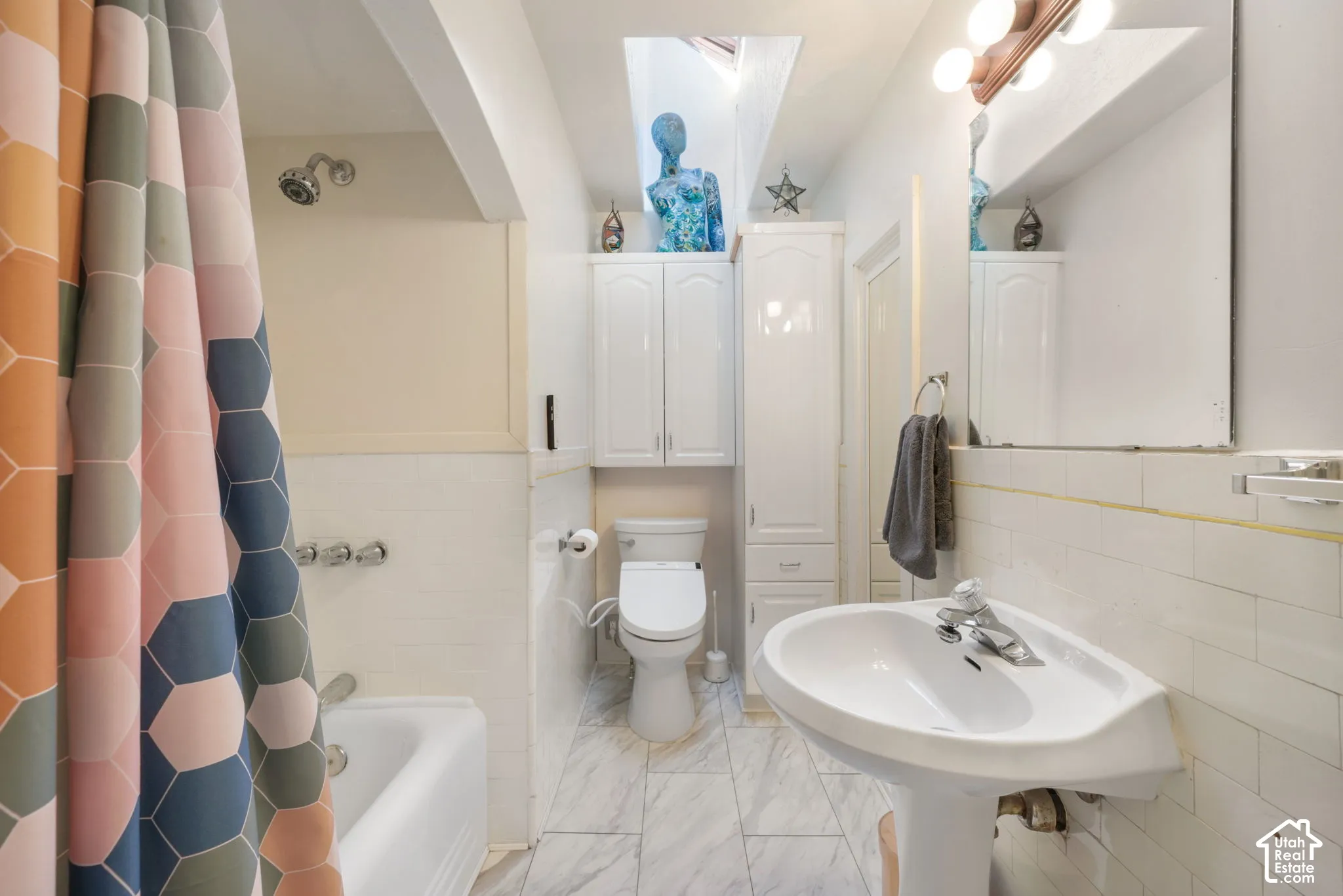 Bathroom featuring a ceiling skylight, white pedestal sink, built-in cabinetry, tile shower surround, and tile flooring