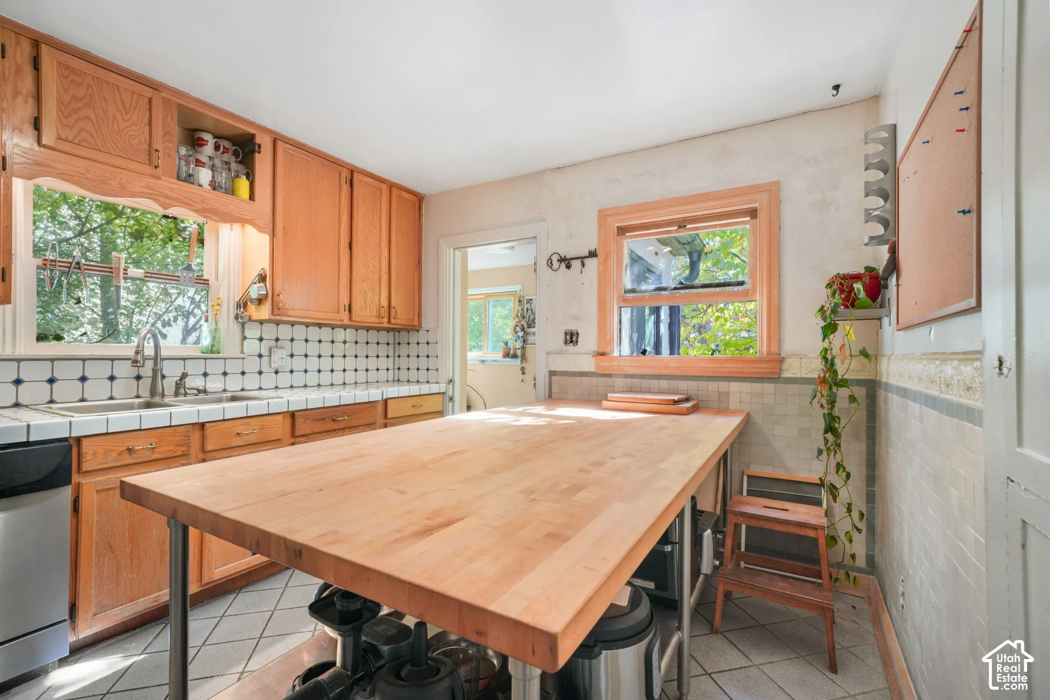 Kitchen featuring wood cabinetry, butcher block island with metal legs, tile backsplash, tile flooring, and dual-basin sink with pull-down faucet