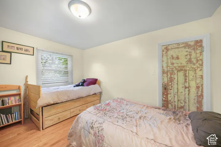 Room featuring wood-finish flooring, a window with horizontal blinds, a flush-mount ceiling light, and an interior door with a multi-panel design