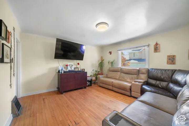 Living space featuring wood-finish flooring, a wall-mounted heater, and a horizontal window with natural light