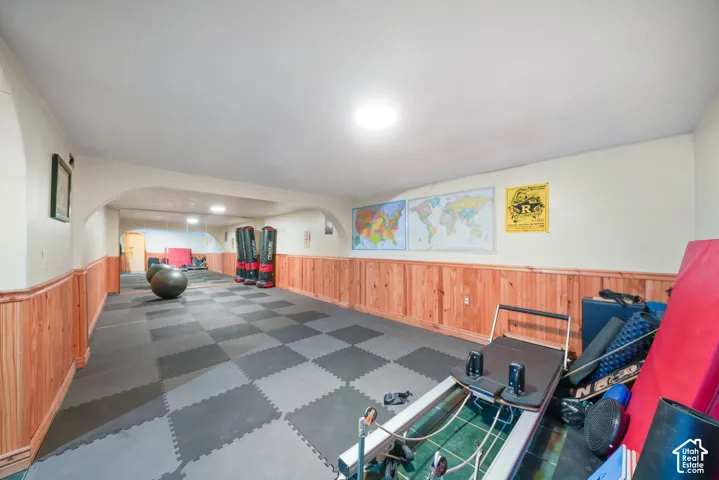Expansive room featuring wood wainscoting, modular rubber flooring, arched architectural detailing, and mirrored wall surfaces