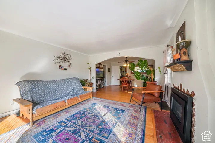 Living area featuring wood-finish flooring, a wall-mounted fireplace insert, a brick hearth, and a decorative archway