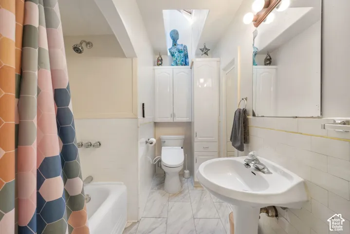 Bathroom featuring a ceiling skylight, white pedestal sink, built-in cabinetry, tile shower surround, and tile flooring