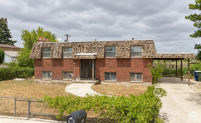 Two-story brick exterior featuring a cedar shake mansard roof, concrete walkway, and an attached carport