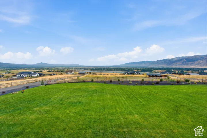 Expansive manicured lawn featuring perimeter split-rail fencing, dark mulch garden beds, and mountain scenery