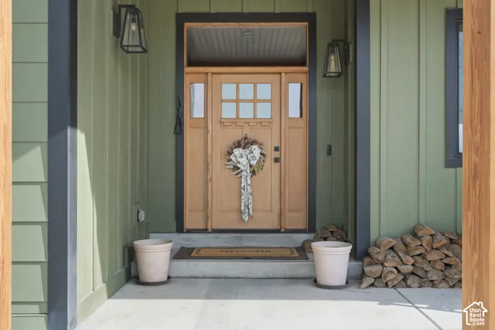 Exterior entry featuring vertical board-and-batten siding, a natural wood-finish front door with an integrated transom window, sidelights, and black geometric wall-mounted light fixtures