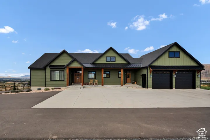 Green lap siding exterior with a covered porch featuring wood support beams, metal roof accents, and a three-car garage