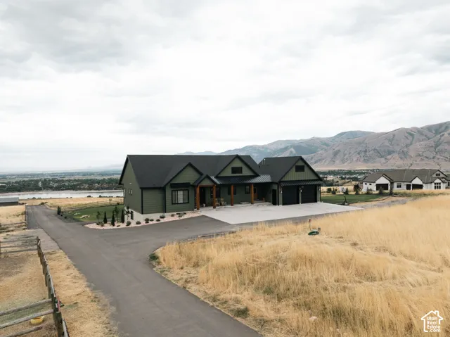 Exterior featuring dark-toned horizontal siding, a gabled roofline, integrated two-car garage, covered entrance with timber columns, and a concrete driveway set against a mountain backdrop