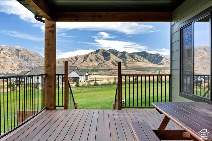 Covered deck with wood-finish decking, natural timber support beams, and metal railing overlooking a landscape featuring mountain terrain