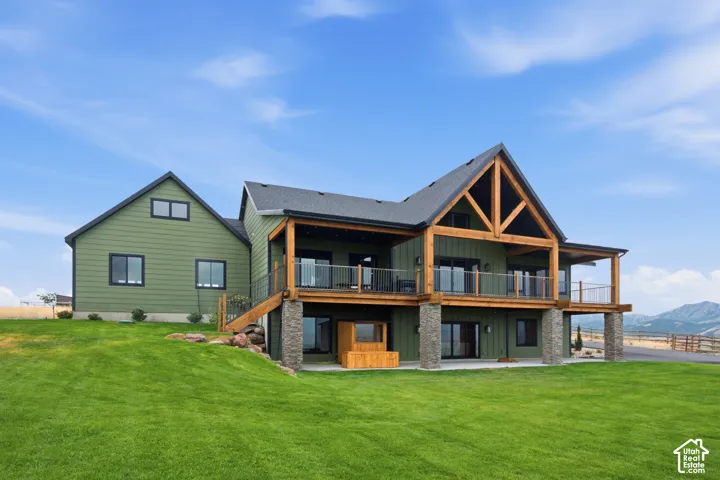 Multi-level residence featuring horizontal lap siding, exposed timber frame accents, stone-clad structural pillars, and a wraparound elevated deck with a metal railing