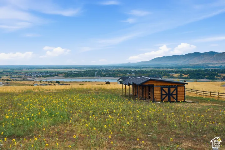 Open acreage featuring native wildflowers, a wood-sided barn with black trim, metal roofing, and mountain-range scenery