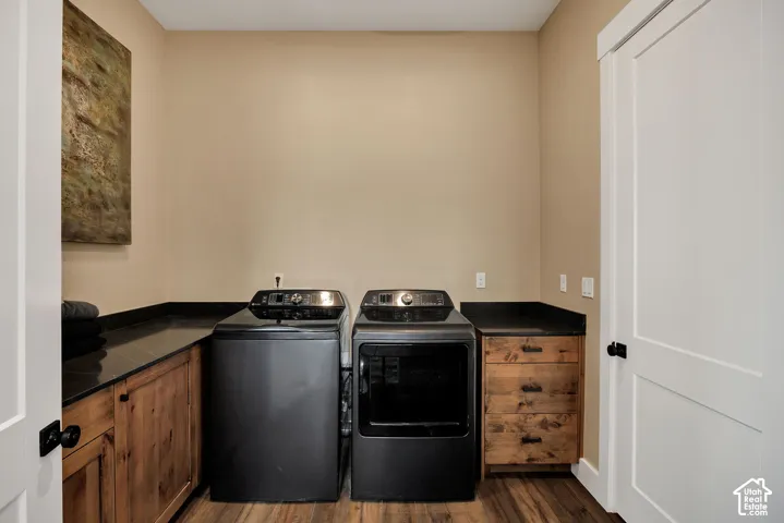 Laundry room featuring custom wood cabinetry, dark stone countertops, wood-finish flooring, and a solid-core panel door with matte black hardware